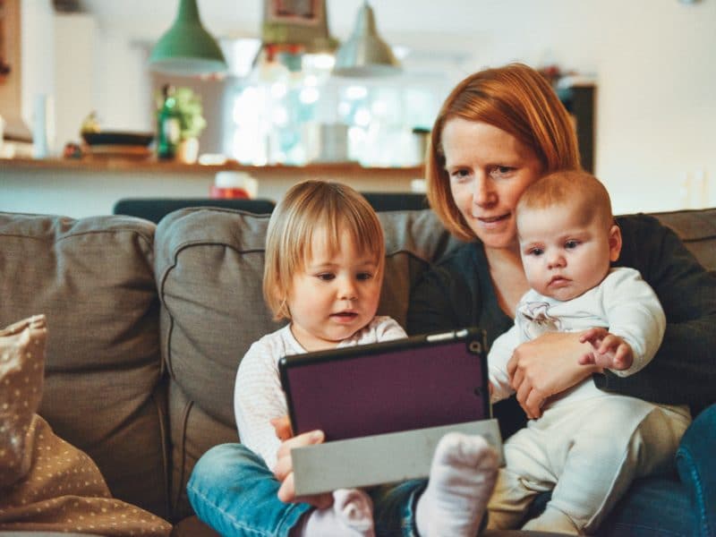 mother-sitting-with-young-kids-on-couch-with-tablet